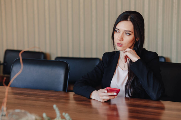 Jonge aantrekkelijke emotionele meisje in Business stijl kleren zittend op Bureau met telefoon in kantoor of publiek - Foto, afbeelding