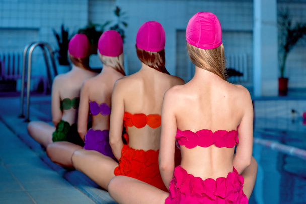 Renkli mayolar ve yüzme havuzunda pembe şapkalar giyen dört güzel, harika, ince, şık bayan.  - Fotoğraf, Görsel