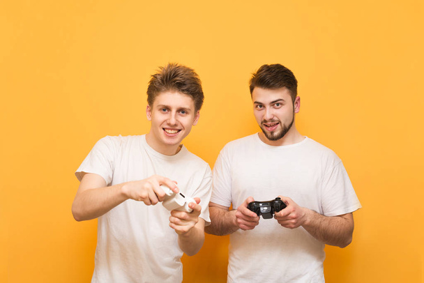 Ystävät joysticks käsissään ovat keltaisella taustalla, katsomalla kameraan ja pelaamalla videopelejä. Kaksi ihmistä pelaa videopelejä konsolilla. Konsolin konseptipeli
. - Valokuva, kuva