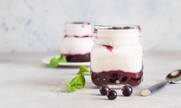 Jars of natural yogurt with berry sauce and mint on light grey table. Healthy eating. Copy space. Summer food concept.  - Foto, Imagem