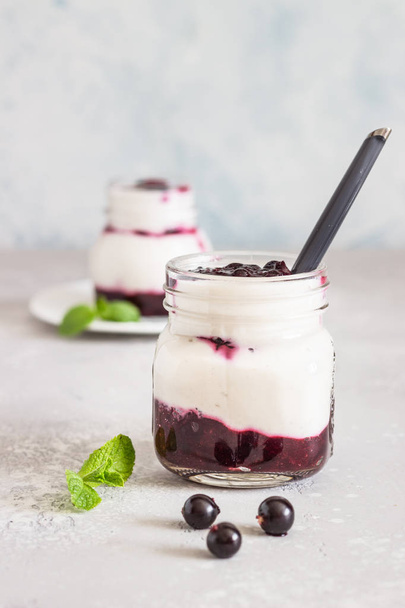 Jars of natural yogurt with berry sauce and mint on light grey table. Healthy eating. Copy space. Summer food concept.  - 写真・画像