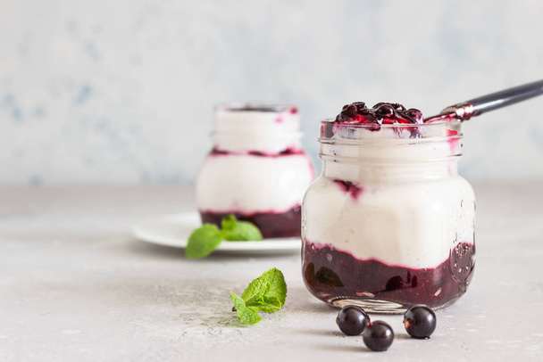 Jars of natural yogurt with berry sauce and mint on light grey table. Healthy eating. Copy space. Summer food concept.  - Foto, imagen