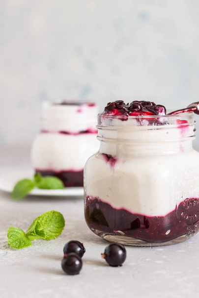 Jars of natural yogurt with berry sauce and mint on light grey table. Healthy eating. Copy space. Summer food concept.  - Foto, Bild