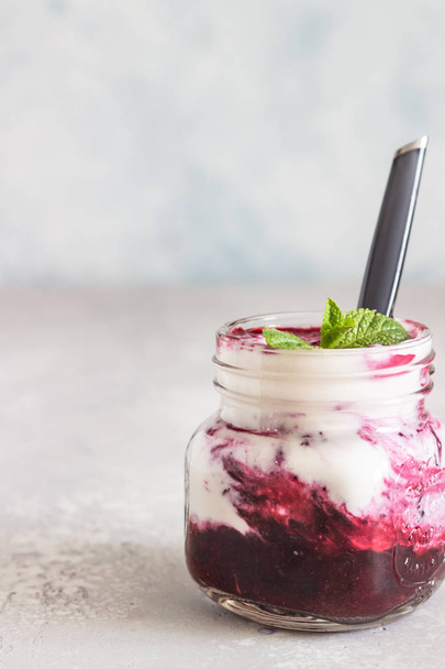 Jars of natural yogurt with berry sauce and mint on light grey table. Healthy eating. Copy space. Summer food concept.  - Fotó, kép