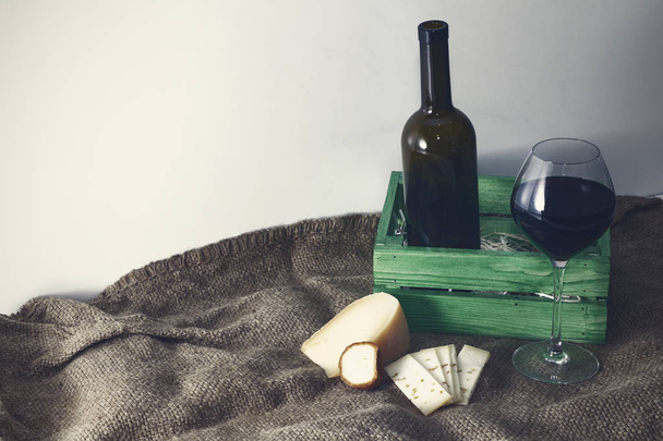 Uma garrafa de vinho tinto com um copo e um pedaço de queijo. - Foto, Imagem
