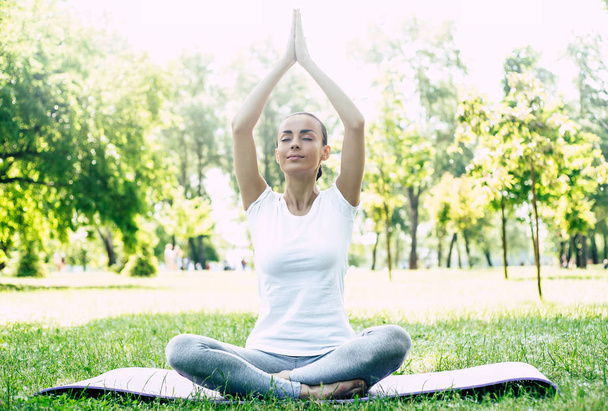 Beautiful young woman doing yoga in park. Relaxing and meditating while being surrounded by nature in summer park - Foto, imagen