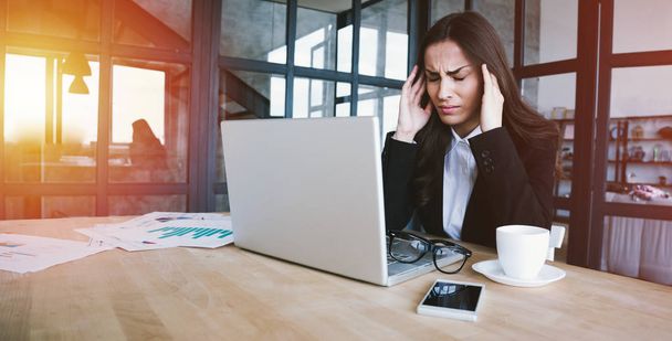 Dużo pracy. Zmęczony kobieta biznesu o ból głowy podczas pracy na swoim laptopie w nowoczesnym biurze  - Zdjęcie, obraz