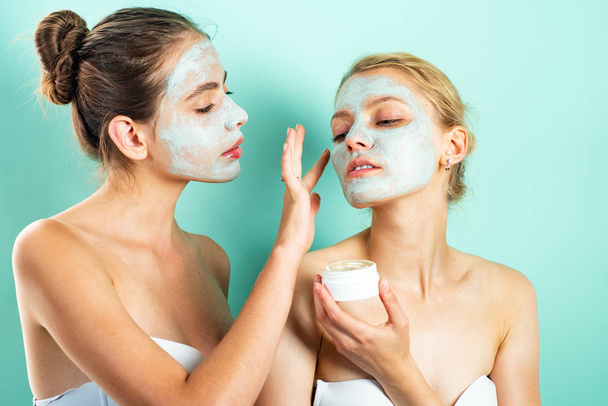 Two young women applying moisturizer cream on their face. Photo of careful friends receiving spa treatments. Home grooming. - 写真・画像