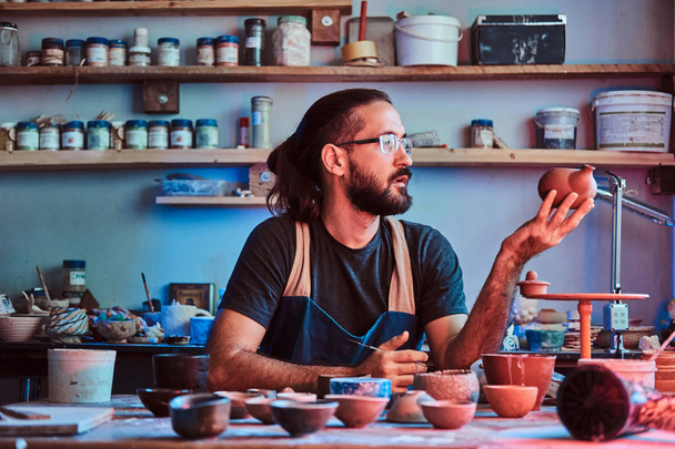 Hardworking man is looking at his own work, ceramic teapot. - Photo, Image
