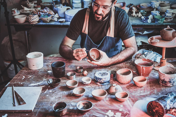 Alfarero pensativo en vasos en su propio taller es workig en una nueva tetera hecha a mano
. - Foto, imagen