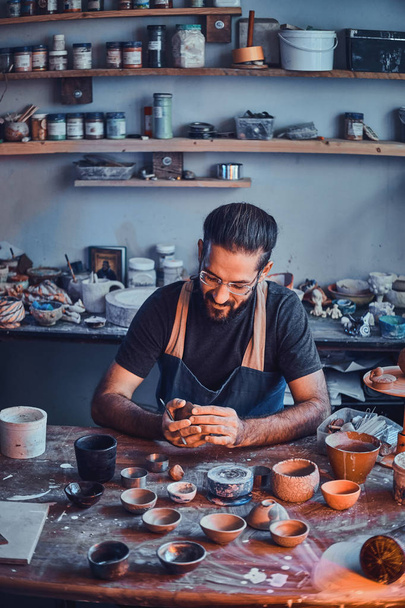 Pensive potter in glasses at his own workshop is workig on a new handmade teapot. - Photo, Image