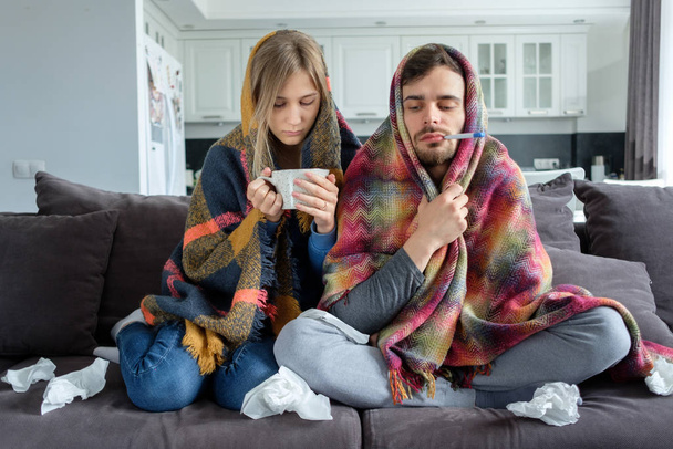 Couple man and woman sick at home, sitting on the couch and wrapped in blankets - Фото, зображення