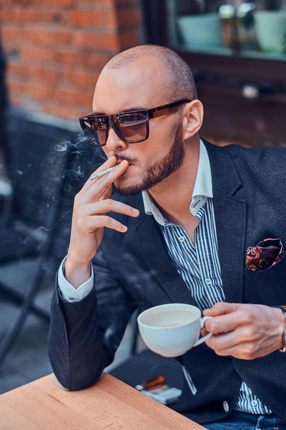 Pensive man is drinking coffee and smoking outside of cafe - Photo, Image