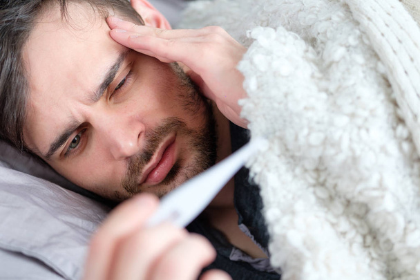 A sick man looks at a thermometer - Photo, image