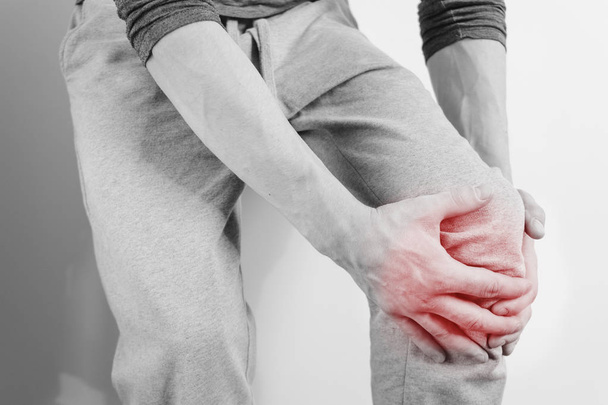 Un hombre sosteniendo su rodilla, dolor en la rodilla. Foto aislada con un punto rojo en el lugar del dolor
. - Foto, Imagen