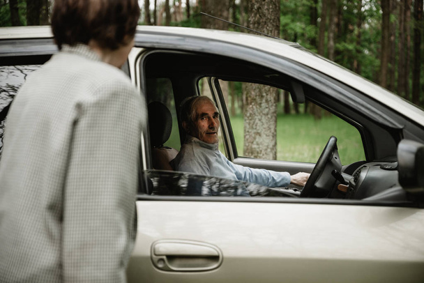 Opa und Oma stehen zusammen in der Natur neben dem Auto. altes Paar, das Spaß an der Natur hat. Senioren mit ihrem neuen Auto. glückliche und schöne alte Menschen - Foto, Bild