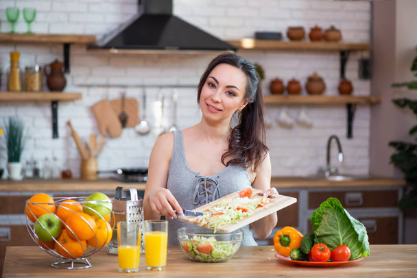 Pretty young woman cutting vegetables salad in the kitchen - Foto, Bild