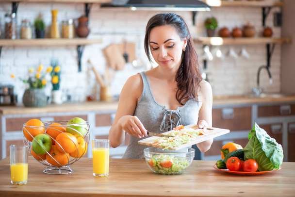 Pretty young woman cutting vegetables salad in the kitchen - Фото, зображення