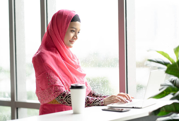 Young arab woman wearing hijab pink dress using laptop computer  - Photo, image
