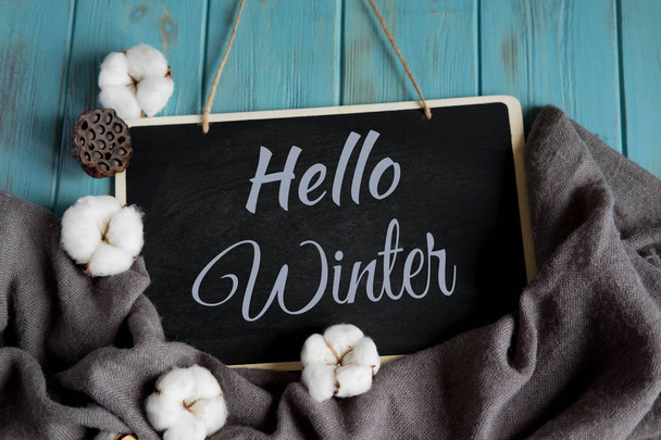 Hello winter postcard. Winter banner with warm gray shawl, cotton flowers on a blue wooden background - Foto, Bild