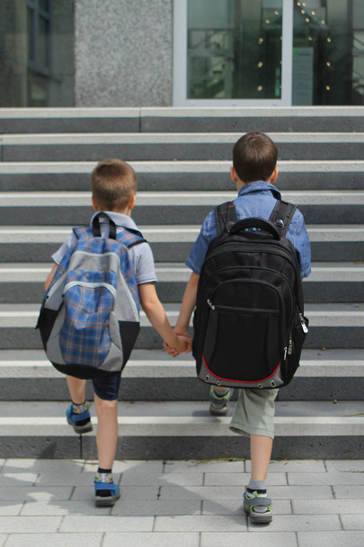 two students, friends, brothers with school backpacks, holding hands, climbing steps to school, Back to school concept, vertical - Фото, изображение