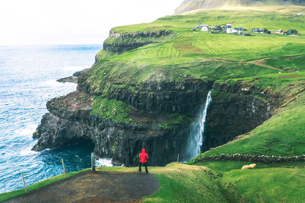 Turista se dívá na vodopád Mulafossur nedaleko Gasadaluru na Faerských ostrovech. - Fotografie, Obrázek