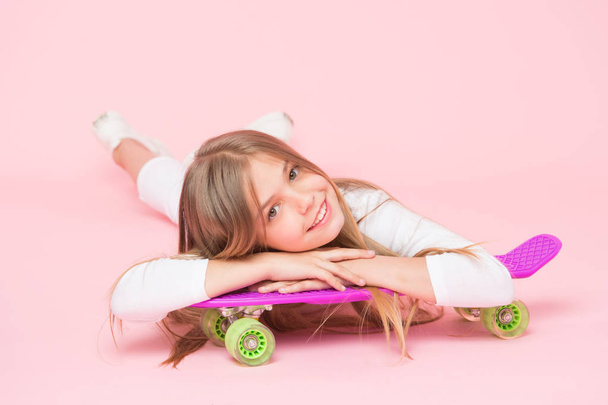 Spreading happy vibrations with the penny board. Small girl skater relaxing at penny board deck on pink background. Little child smiling with violet penny board. Happy hipster with penny skateboard - 写真・画像