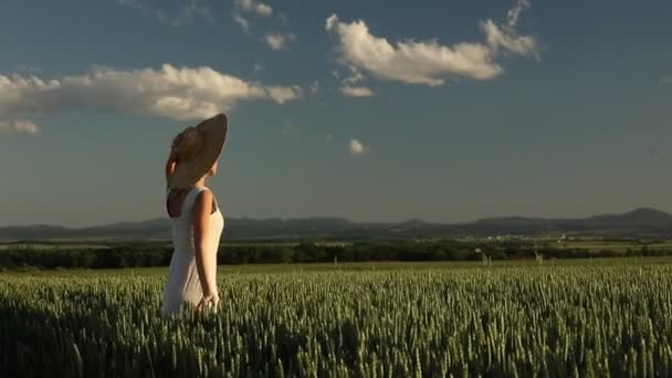 young girl in hat on a green wheat field and mountains on background - Footage, Video
