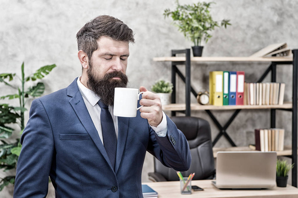 Drinking coffee relaxing break. Boss enjoying energy drink. Start day with coffee. Successful people drink coffee. Caffeine addicted. Man bearded businessman hold coffee cup stand office background - Fotografie, Obrázek