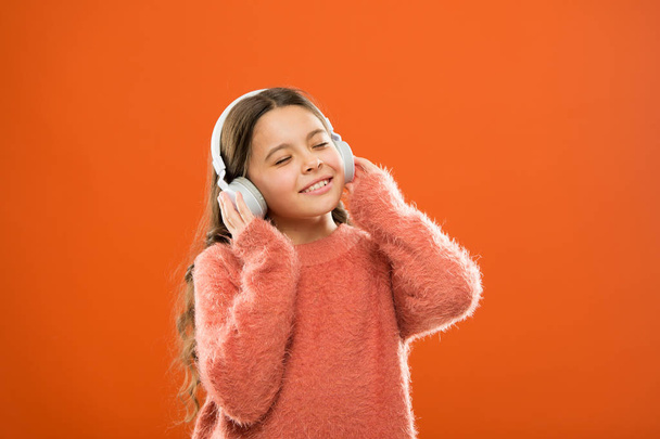 Girl cute little child wear headphones listen music. Kid listen music orange background. Recommended music based on initial interest. Best free music apps for your mobile device. Enjoy sound - Foto, Imagem