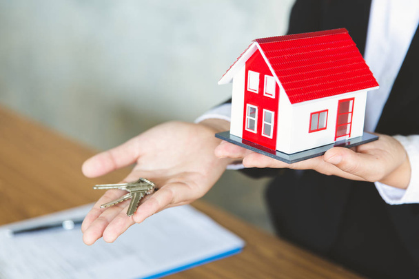 Agente imobiliário segurando modelo de casa e chaves, sinalização do cliente
 - Foto, Imagem