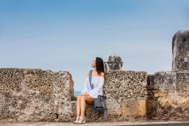 Beautiful woman on white dress sitting alone at the walls surrounding the colonial city of Cartagena de Indias - 写真・画像