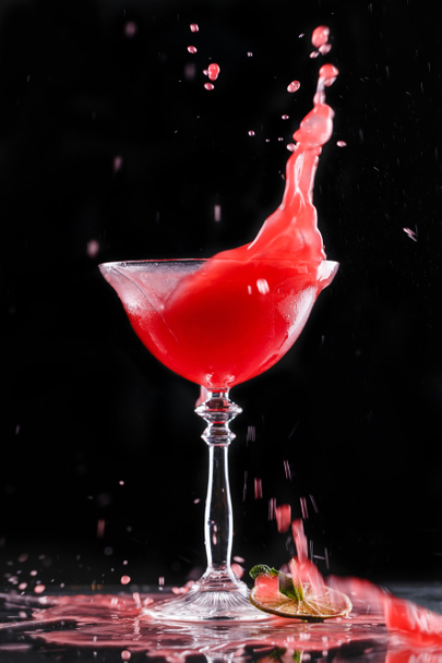 Kalter roter Cocktail mit Früchten im hohen Glas auf schwarzem Hintergrund. Sommergetränke und alkoholische Cocktails, Splash in Bewegung. - Foto, Bild