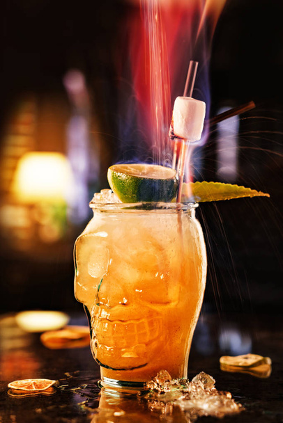 Flamme über Zitrusfrüchten alkoholisches Getränk mit Limette und Eis im Glas der geformten Schädel Hintergrund der Restaurant-Atmosphäre. Sommergetränke und Cocktails, Spritzer und Tropfen - Foto, Bild