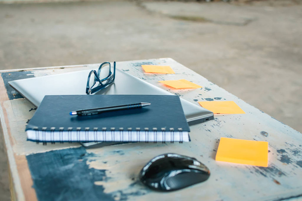 Caneta, caderno, caneta, laptop, mouse, óculos e adesivos na mesa
. - Foto, Imagem