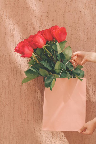 beautiful bouquet of roses in a pastel pink package in women's hands against rough wall - Foto, Bild