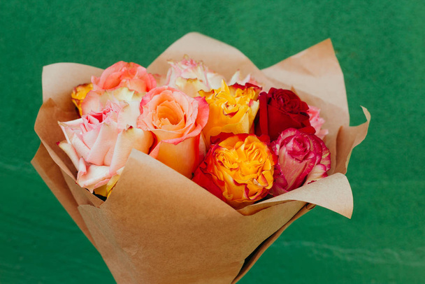 delicate beautiful bouquet of fresh colorful roses packed in craft paper in front of the green wall - Фото, зображення