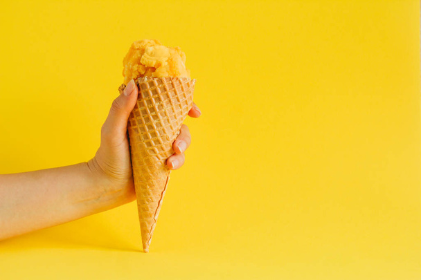 female hand holding waffle cone ice cream isolated on a vibrant yellow background, copy space - Foto, immagini