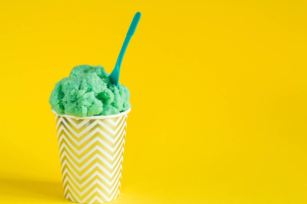 green fruit ice cream or frozen yogurt in stripped  a cup with a spoon on a yellow background copy  space - Valokuva, kuva