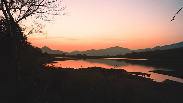 Paisaje con naranja y púrpura al atardecer siluetas de montañas, colinas y lago del bosque
 - Foto, imagen