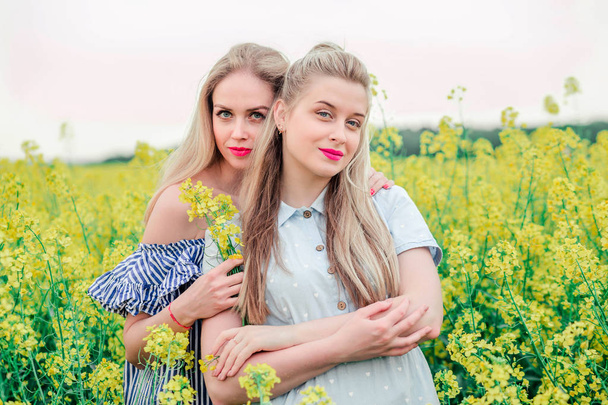 две девушки модели позируют вместе на камере в поле рапса
 - Фото, изображение