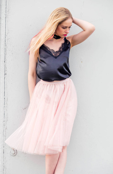fashionable girl model in a tulle skirt and black top posing against a gray wall - Fotó, kép