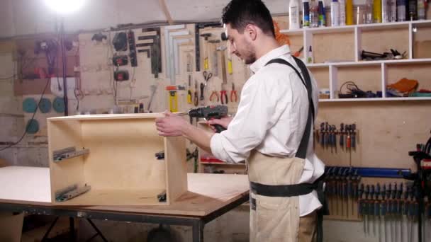 Konzept von Geschäft und Produktion. Junger Mann in der Werkstatt montiert Möbel - Filmmaterial, Video