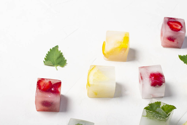 Ice cubes with fruit and mint leaves on a white stone background - Foto, afbeelding