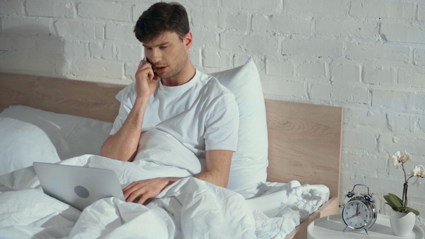 yatakta yatan beyaz t-shirt freelancer, akıllı telefon konuşuyor ve sabah dizüstü bilgisayar ile çalışma - Video, Çekim