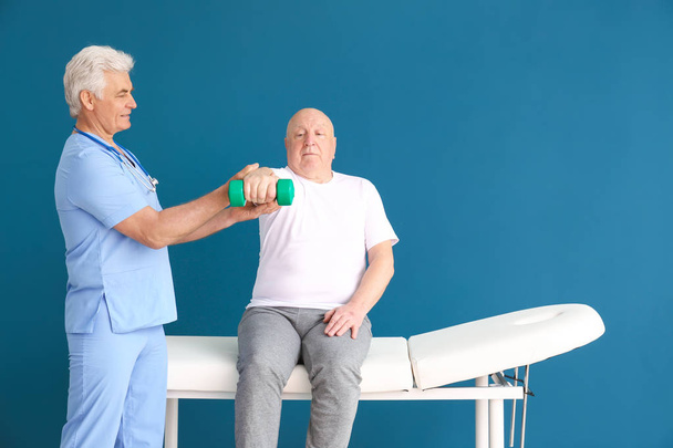 Zralá fyzioterapeutka pracující s vrchním mužem na barevném pozadí - Fotografie, Obrázek