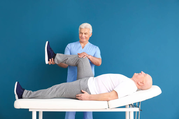 Mature physiotherapist working with senior man on color background - Фото, изображение