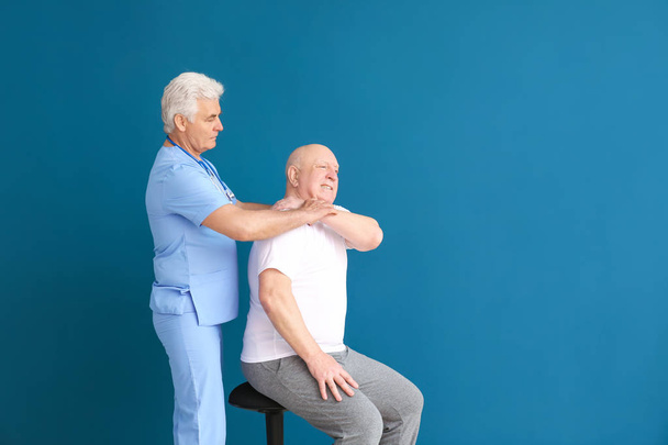 Ältere Physiotherapeutin arbeitet mit älteren Mann an Farbhintergrund - Foto, Bild