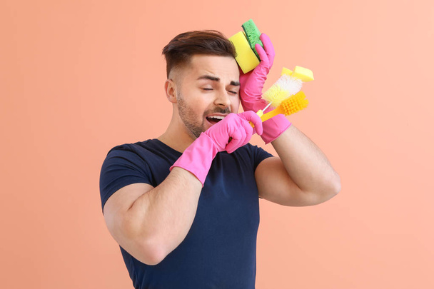 Tired young man with cleaning supplies on color background - Valokuva, kuva