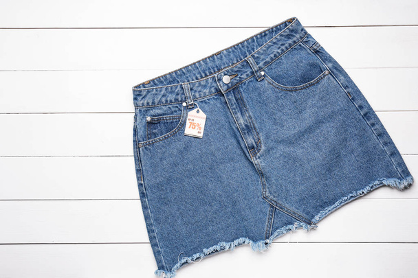 Stylowa spódnica jeansowa z tagiem na białym tle drewnianym - Zdjęcie, obraz